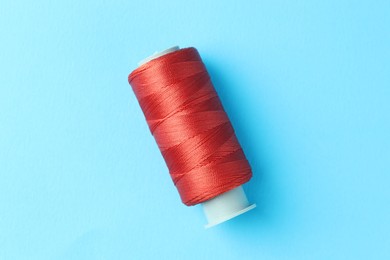 Photo of Spool of red sewing thread on light blue background, top view