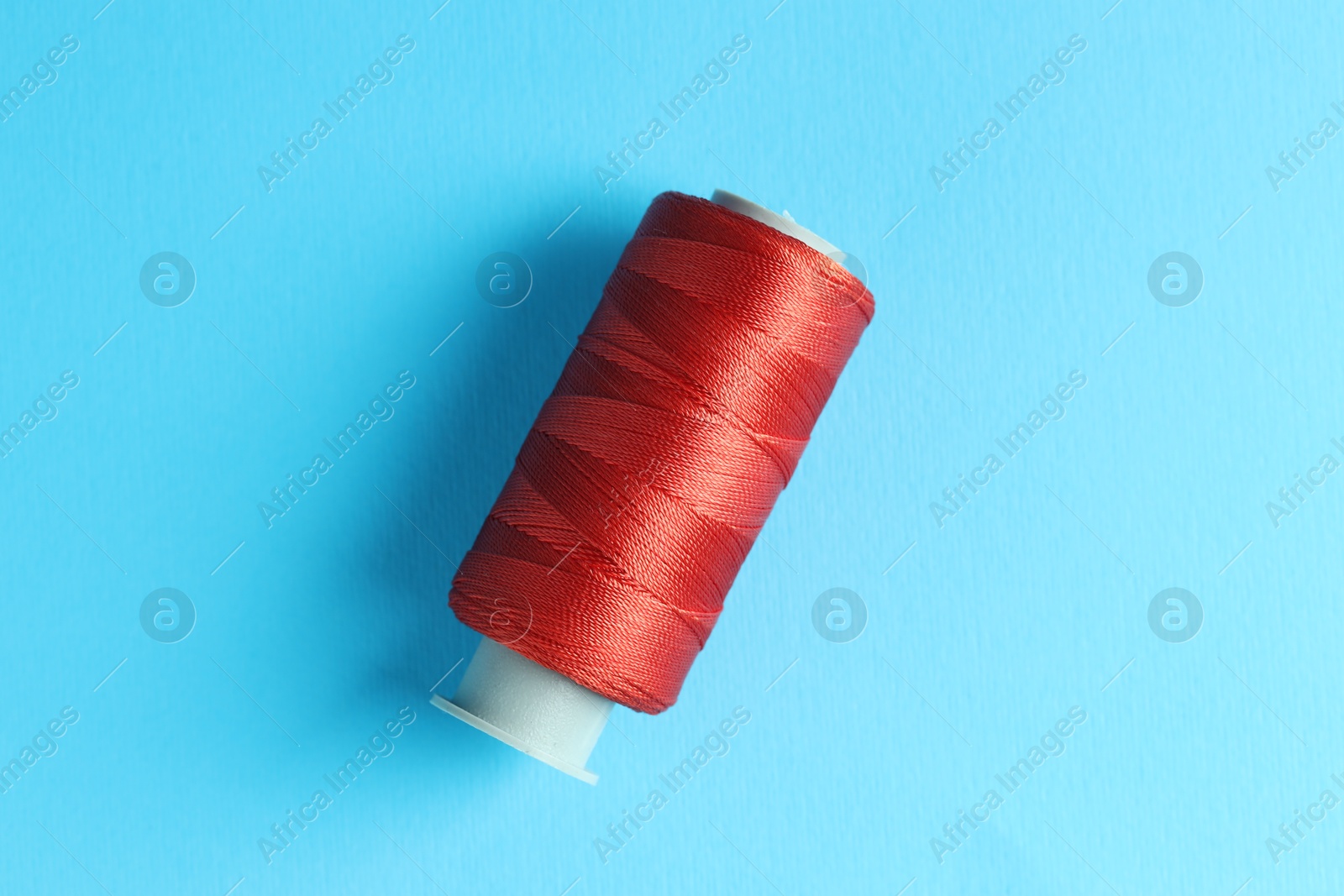 Photo of Spool of red sewing thread on light blue background, top view