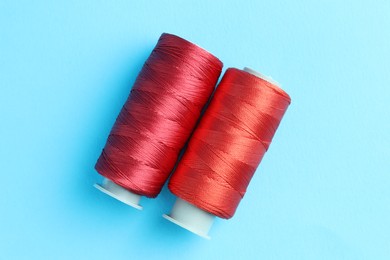 Photo of Spools of red sewing threads on light blue background, top view