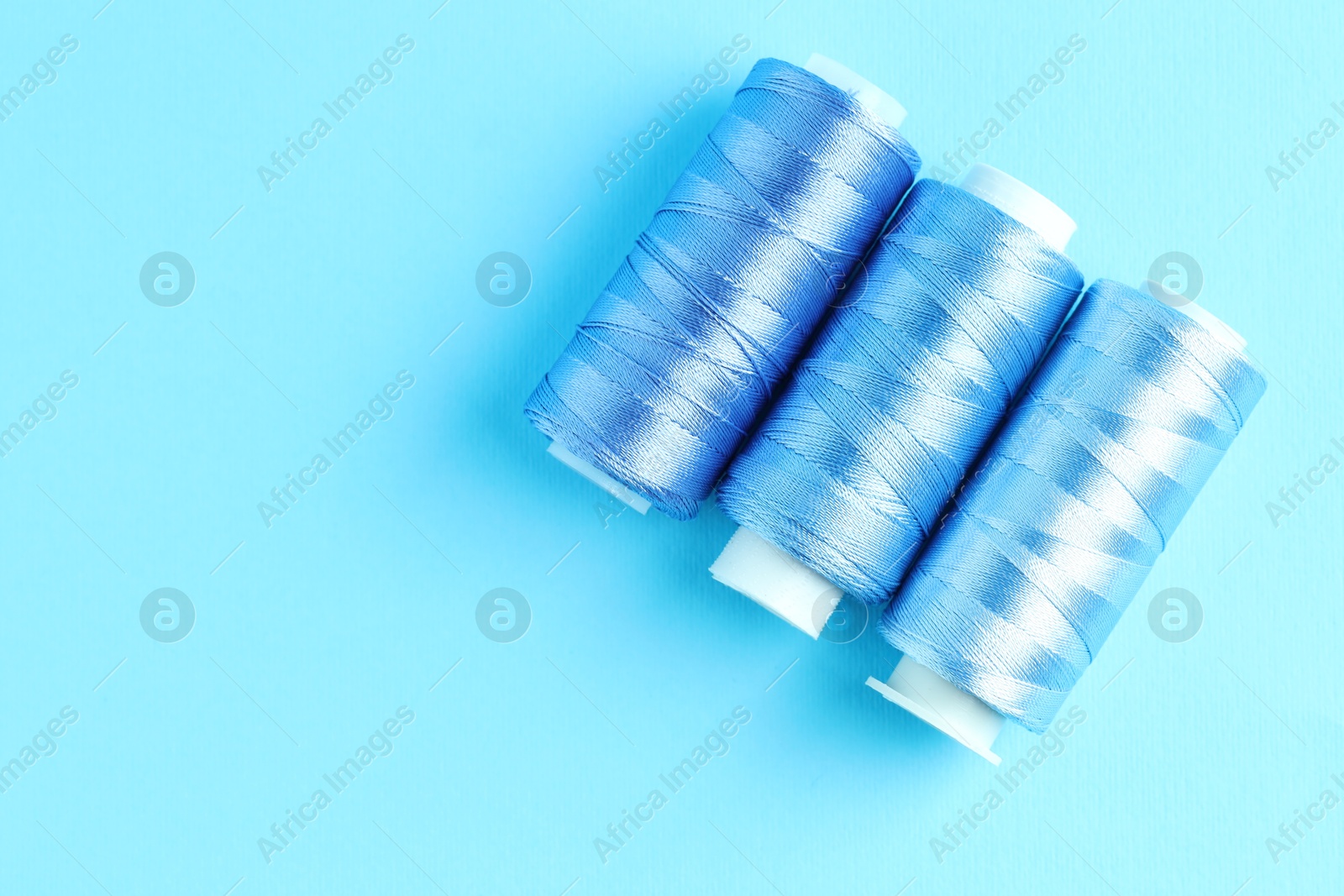 Photo of Spools of colorful sewing threads on light blue background, flat lay. Space for text