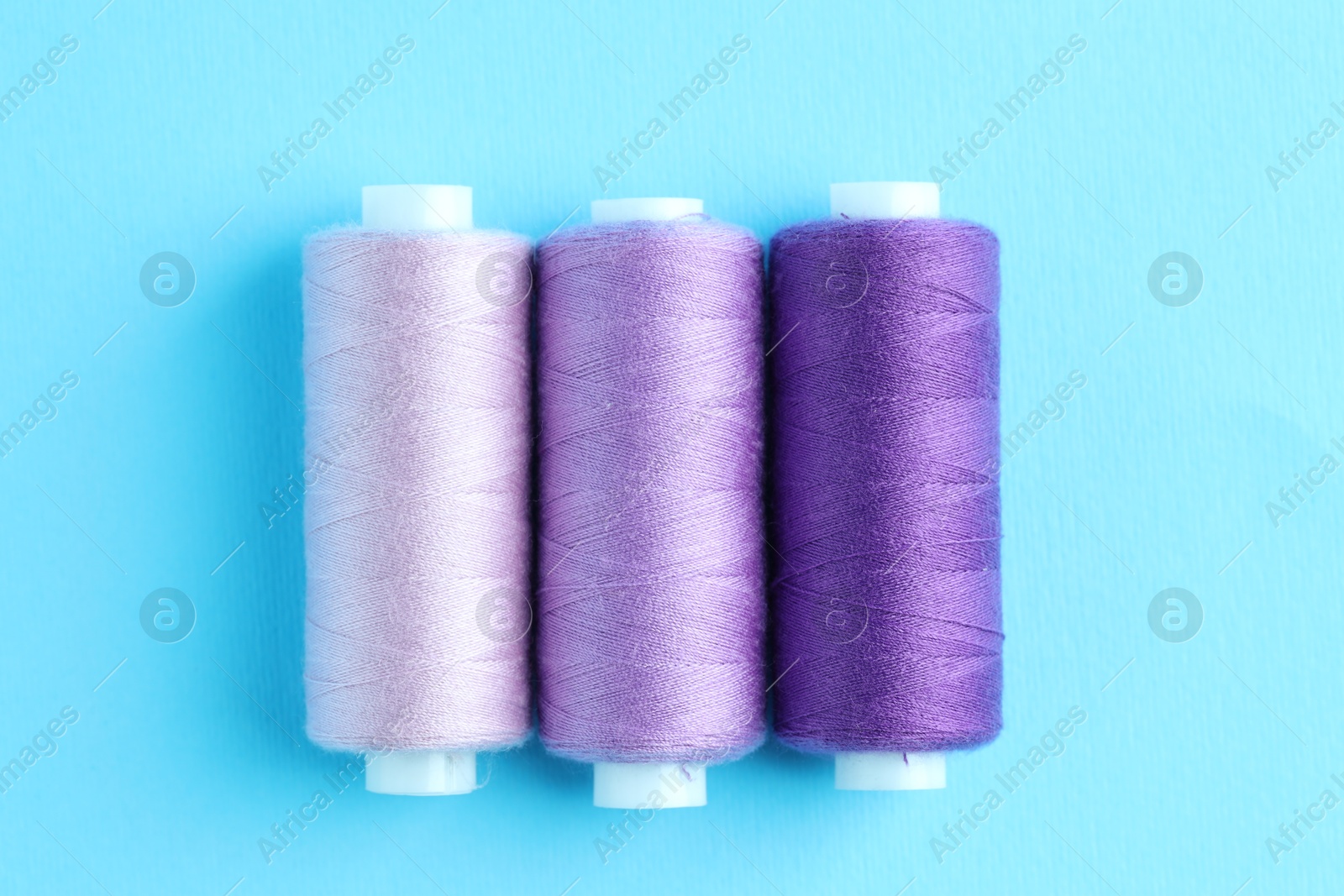 Photo of Spools of colorful sewing threads on light blue background, flat lay