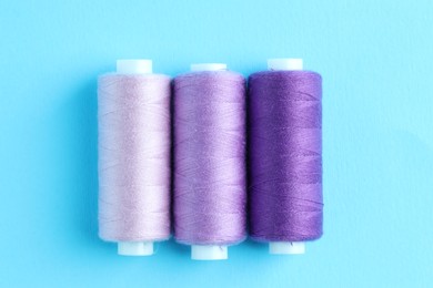 Photo of Spools of colorful sewing threads on light blue background, flat lay