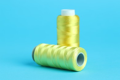 Photo of Spools of yellow sewing threads on light blue background, closeup