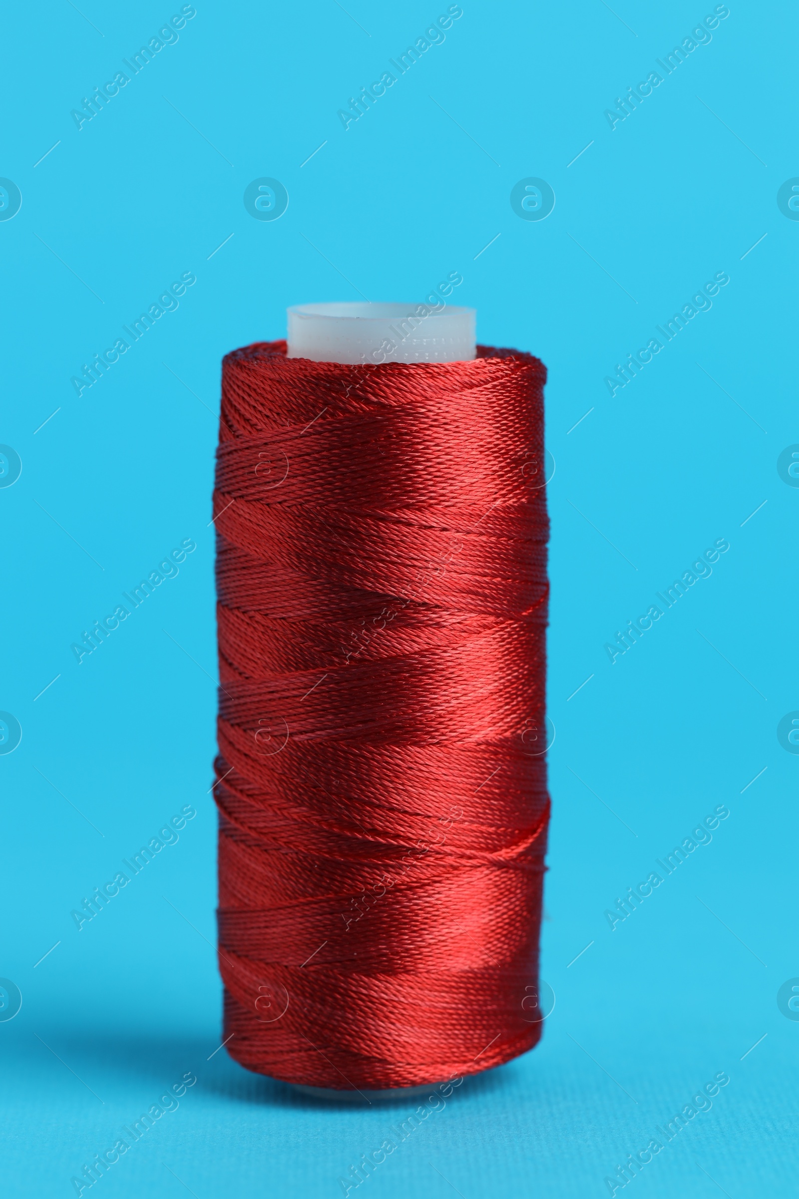 Photo of Spool of red sewing thread on light blue background