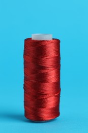 Photo of Spool of red sewing thread on light blue background