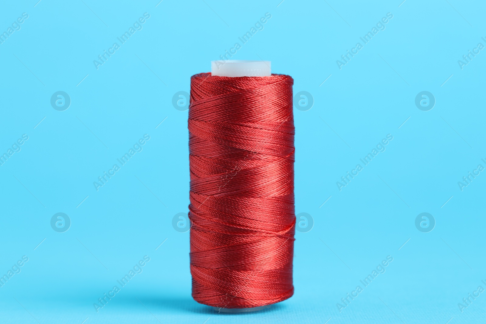 Photo of Spool of red sewing thread on light blue background