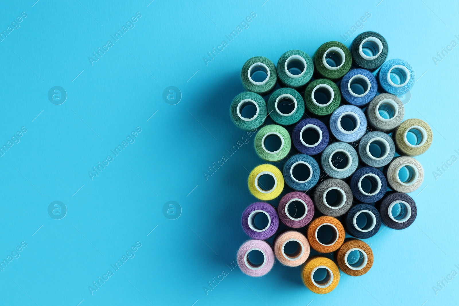 Photo of Spools of colorful sewing threads on light blue background, flat lay. Space for text