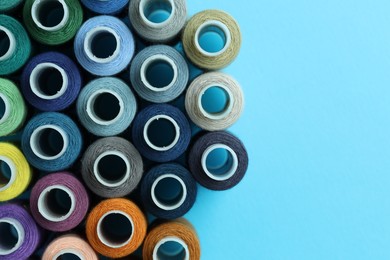 Photo of Spools of colorful sewing threads on light blue background, flat lay. Space for text