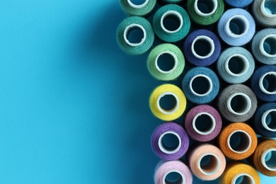 Photo of Spools of colorful sewing threads on light blue background, flat lay. Space for text