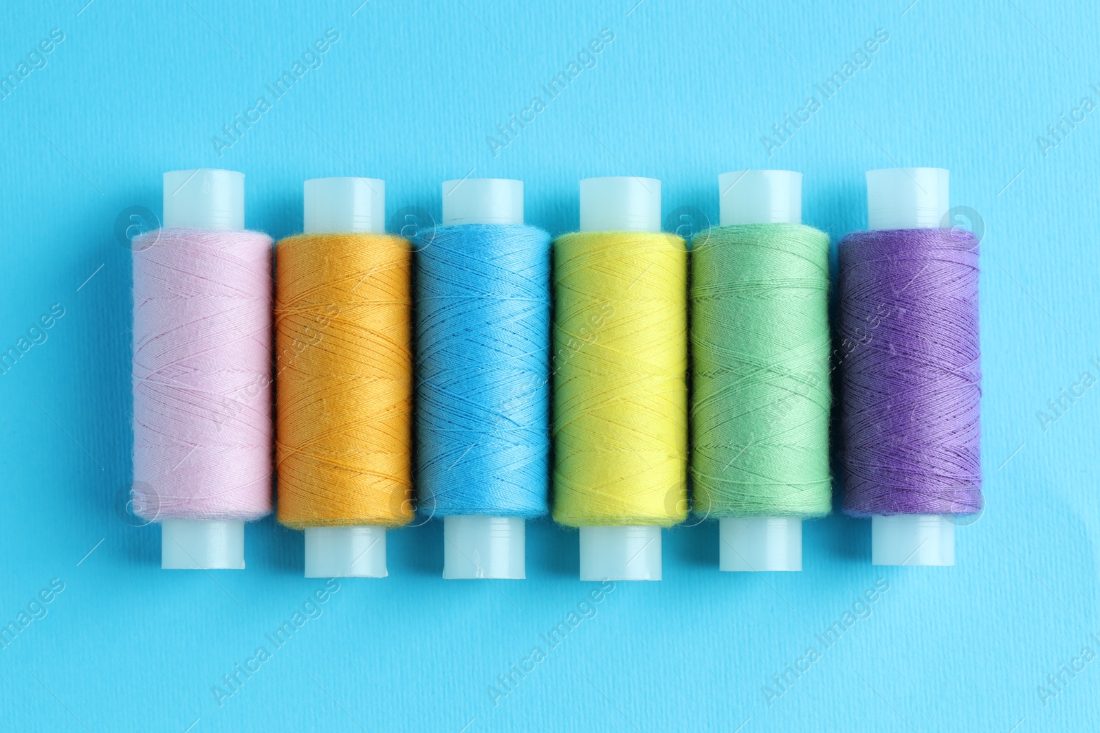 Photo of Spools of colorful sewing threads on light blue background, flat lay