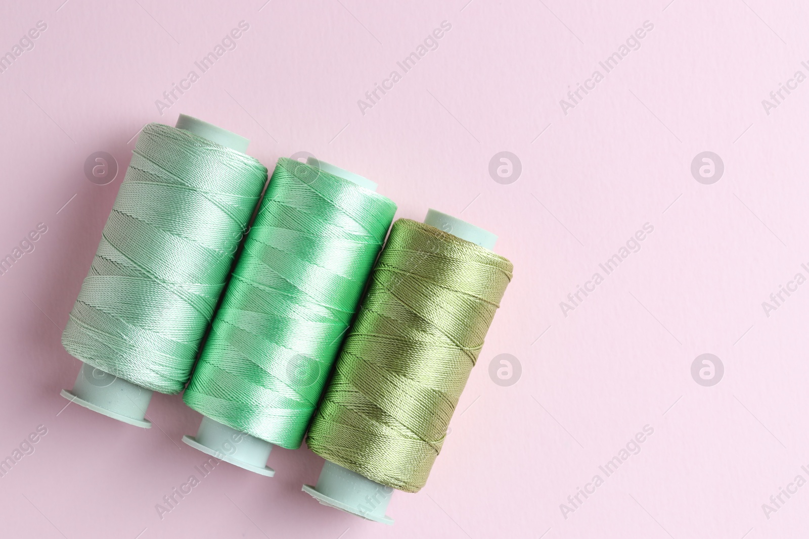 Photo of Spools of colorful sewing threads on pink background, flat lay. Space for text