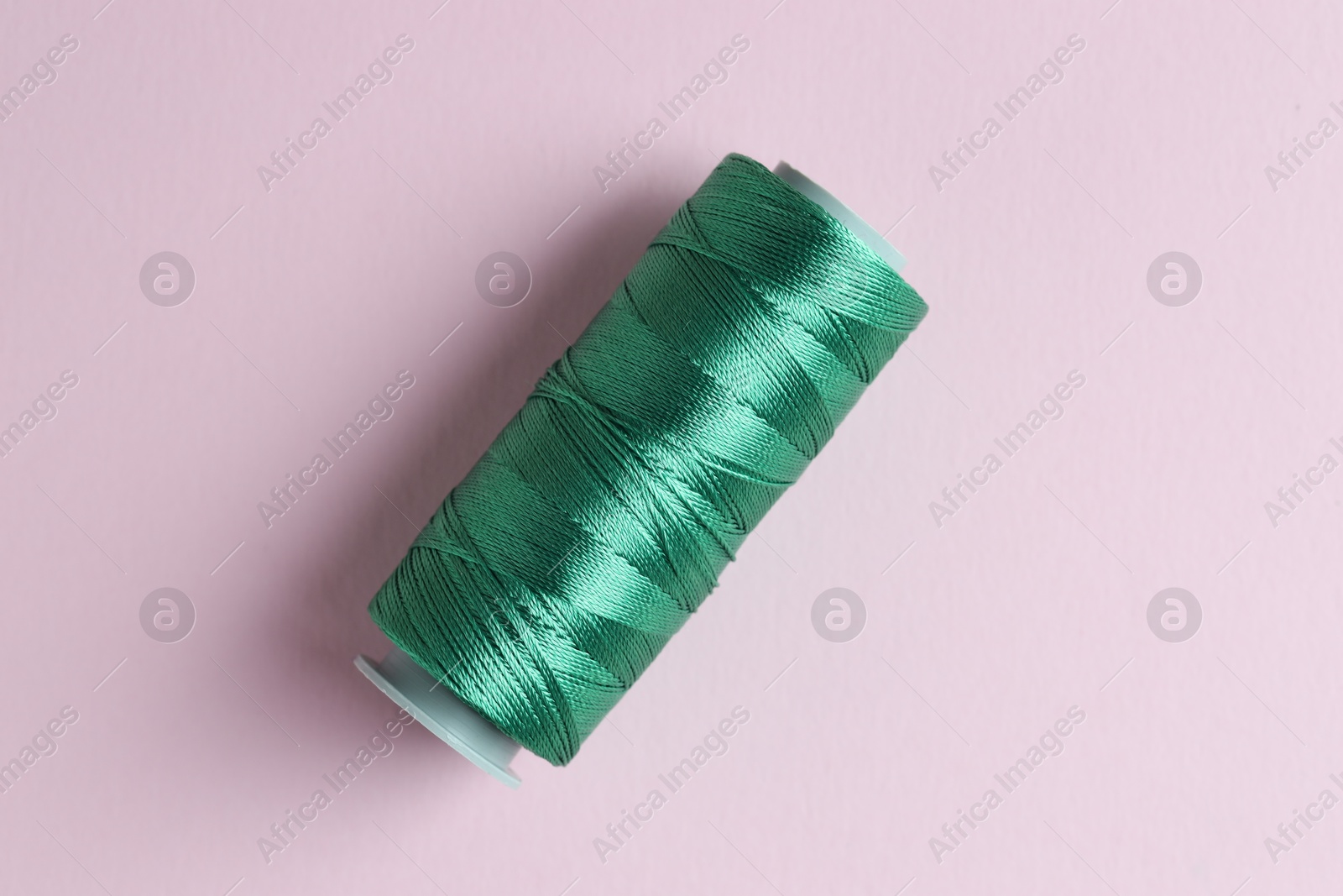 Photo of Spool of green sewing thread on pink background, top view