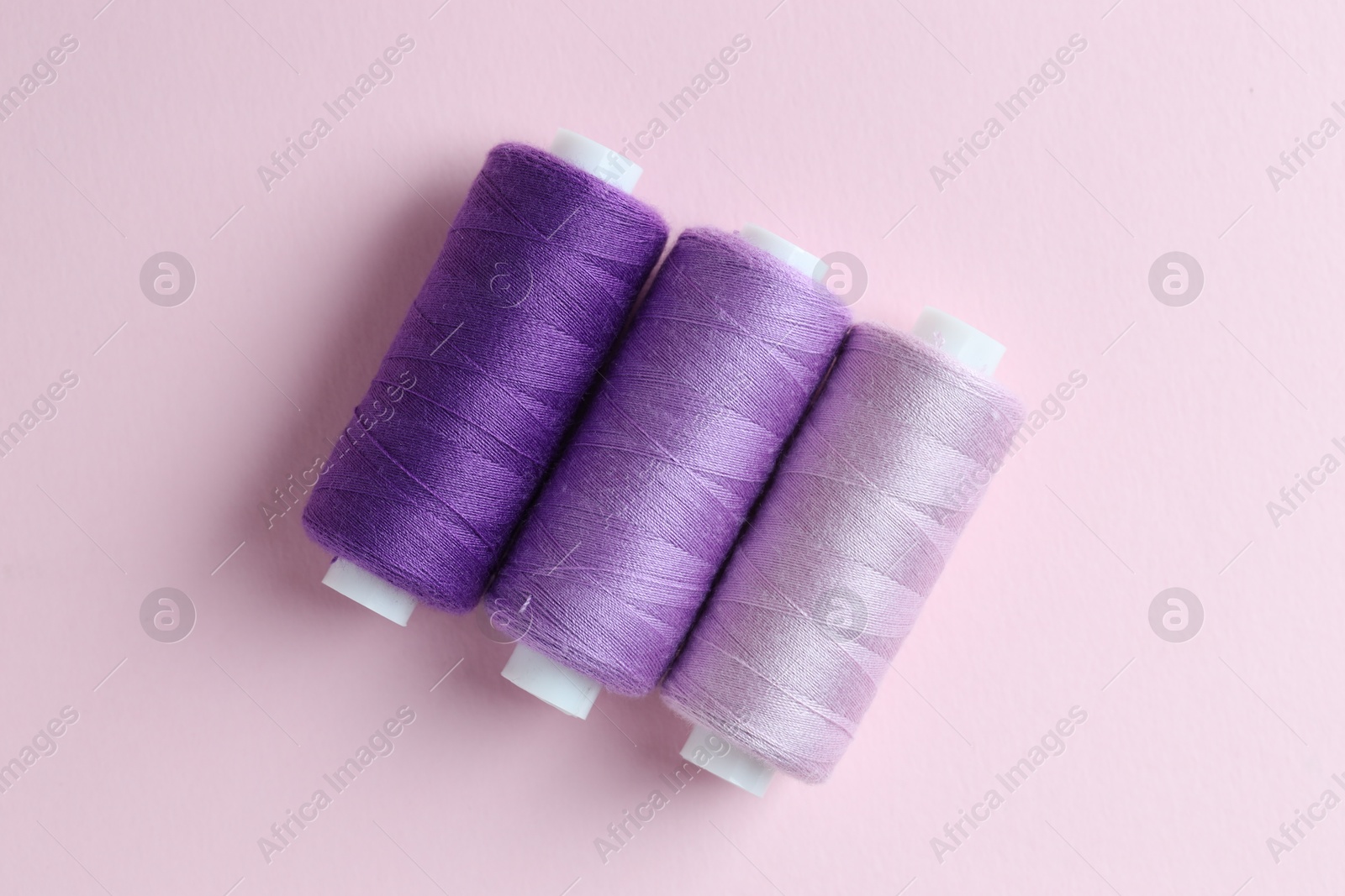 Photo of Spools of colorful sewing threads on pink background, flat lay