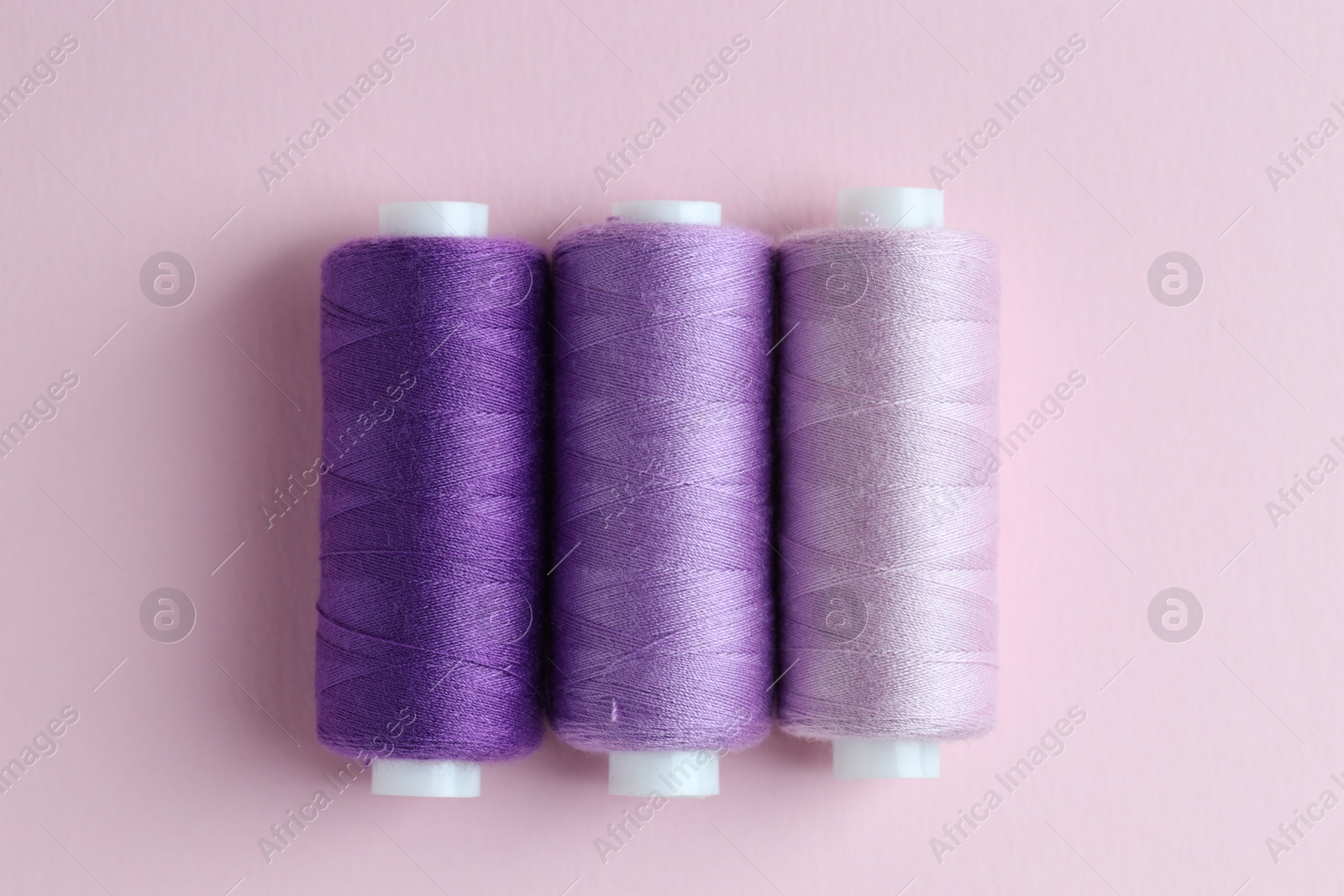 Photo of Spools of colorful sewing threads on pink background, flat lay