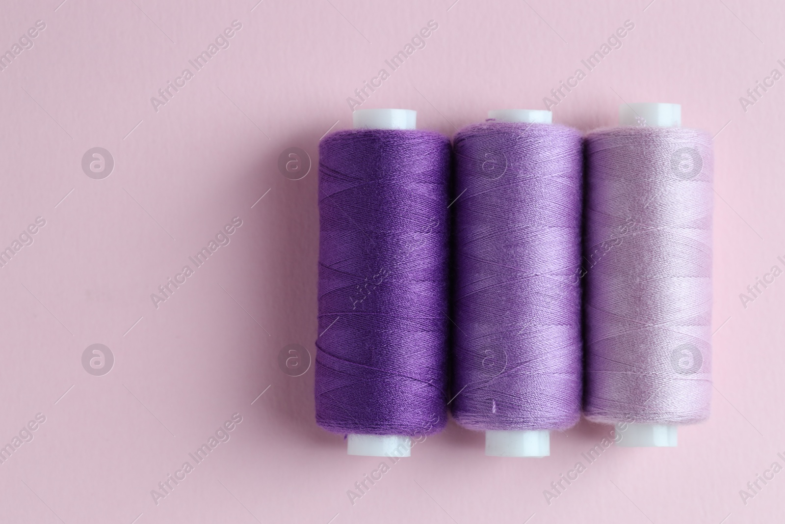 Photo of Spools of colorful sewing threads on pink background, flat lay. Space for text