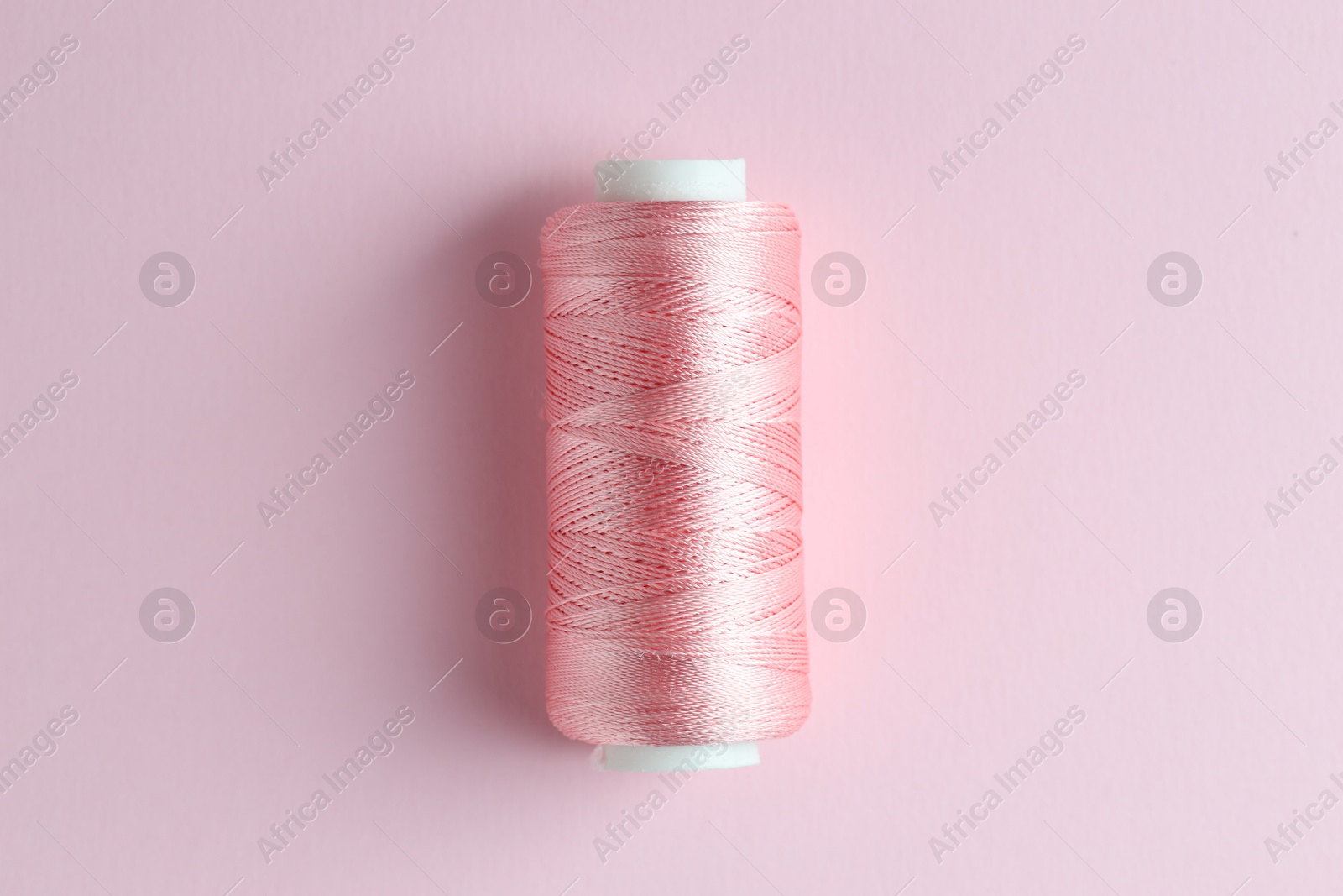 Photo of Spool of sewing thread on pink background, top view