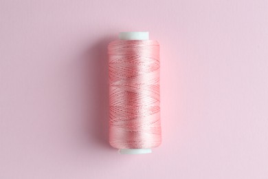 Photo of Spool of sewing thread on pink background, top view