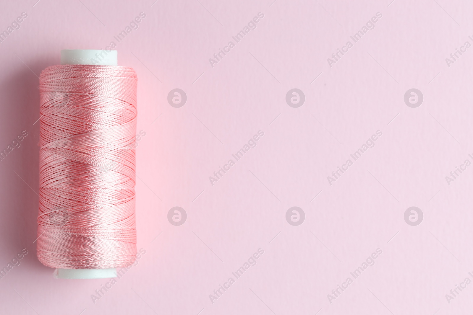 Photo of Spool of sewing thread on pink background, top view. Space for text