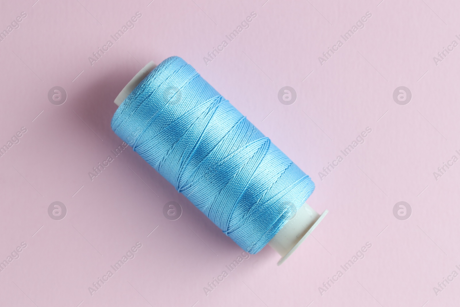 Photo of Spool of light blue sewing thread on pink background, top view