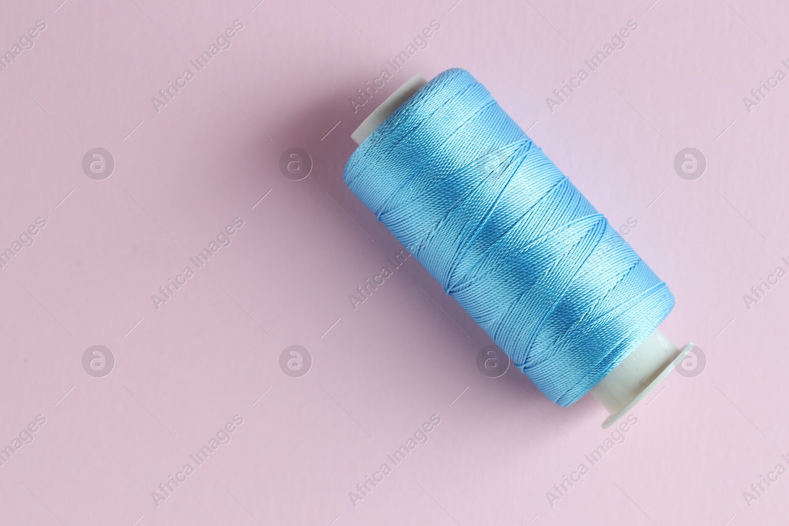 Photo of Spool of light blue sewing thread on pink background, top view. Space for text