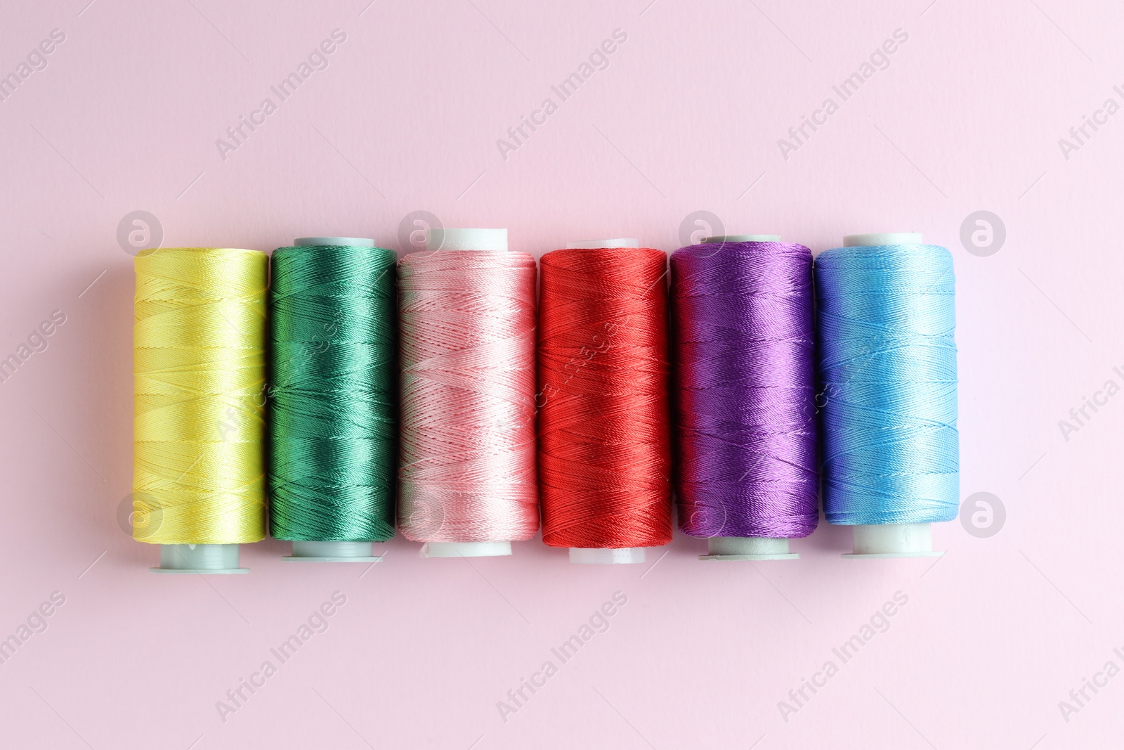 Photo of Spools of colorful sewing threads on pink background, flat lay