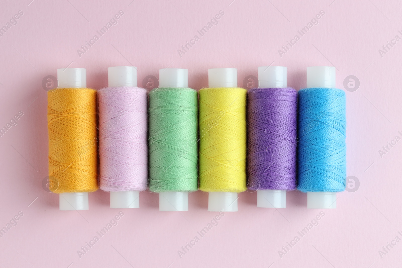 Photo of Spools of colorful sewing threads on pink background, flat lay