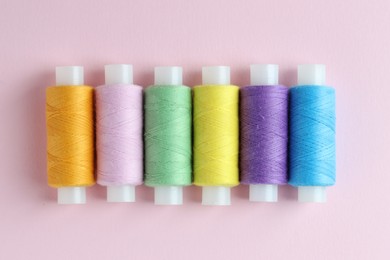 Photo of Spools of colorful sewing threads on pink background, flat lay