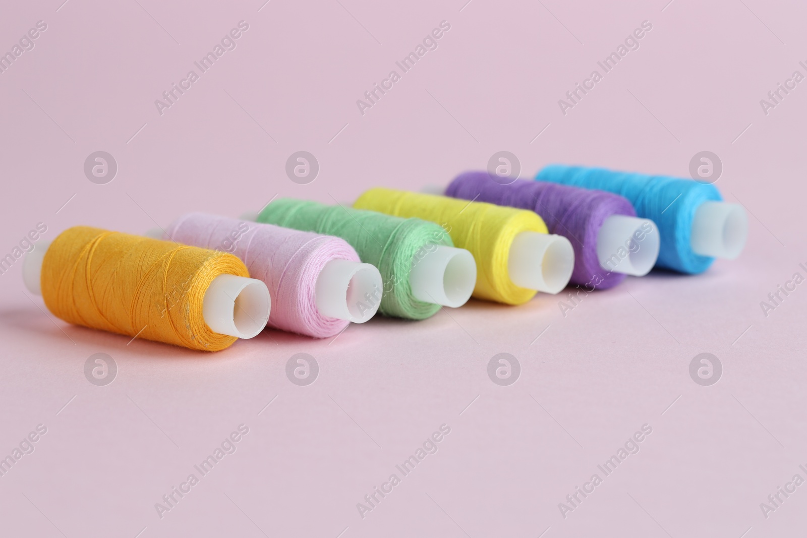 Photo of Spools of colorful sewing threads on pink background, closeup