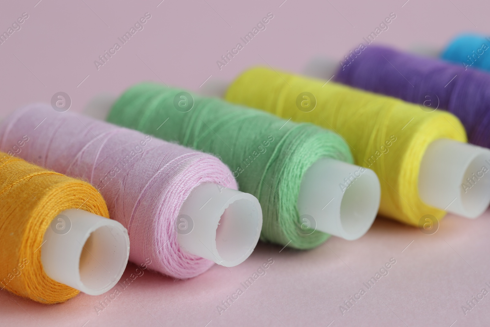 Photo of Spools of colorful sewing threads on pink background, closeup