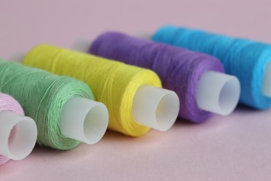 Photo of Spools of colorful sewing threads on pink background, closeup