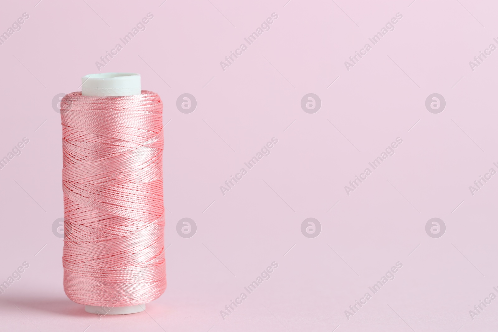 Photo of Spool of sewing thread on pink background, space for text