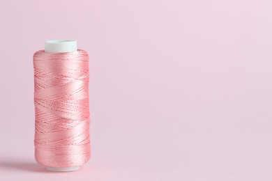 Photo of Spool of sewing thread on pink background, space for text