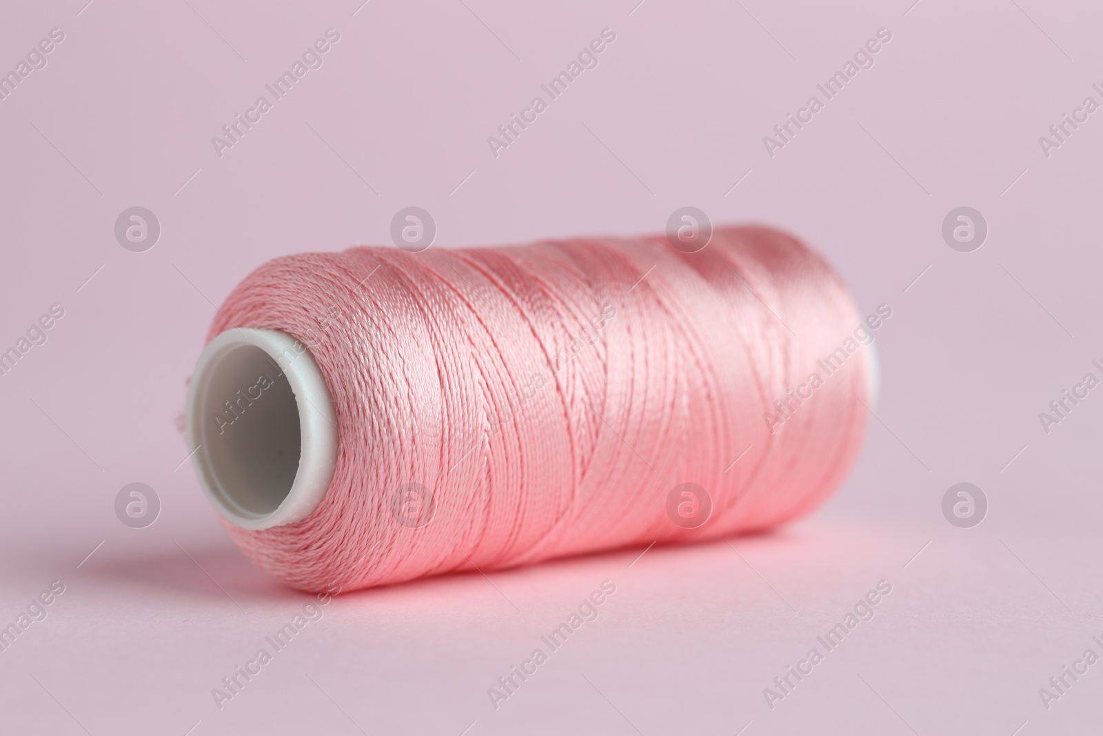 Photo of Spool of sewing thread on pink background, closeup