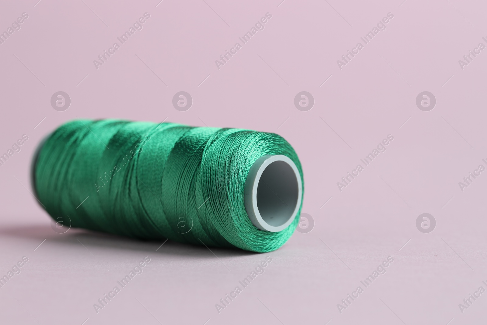 Photo of Spool of green sewing thread on pink background, closeup. Space for text