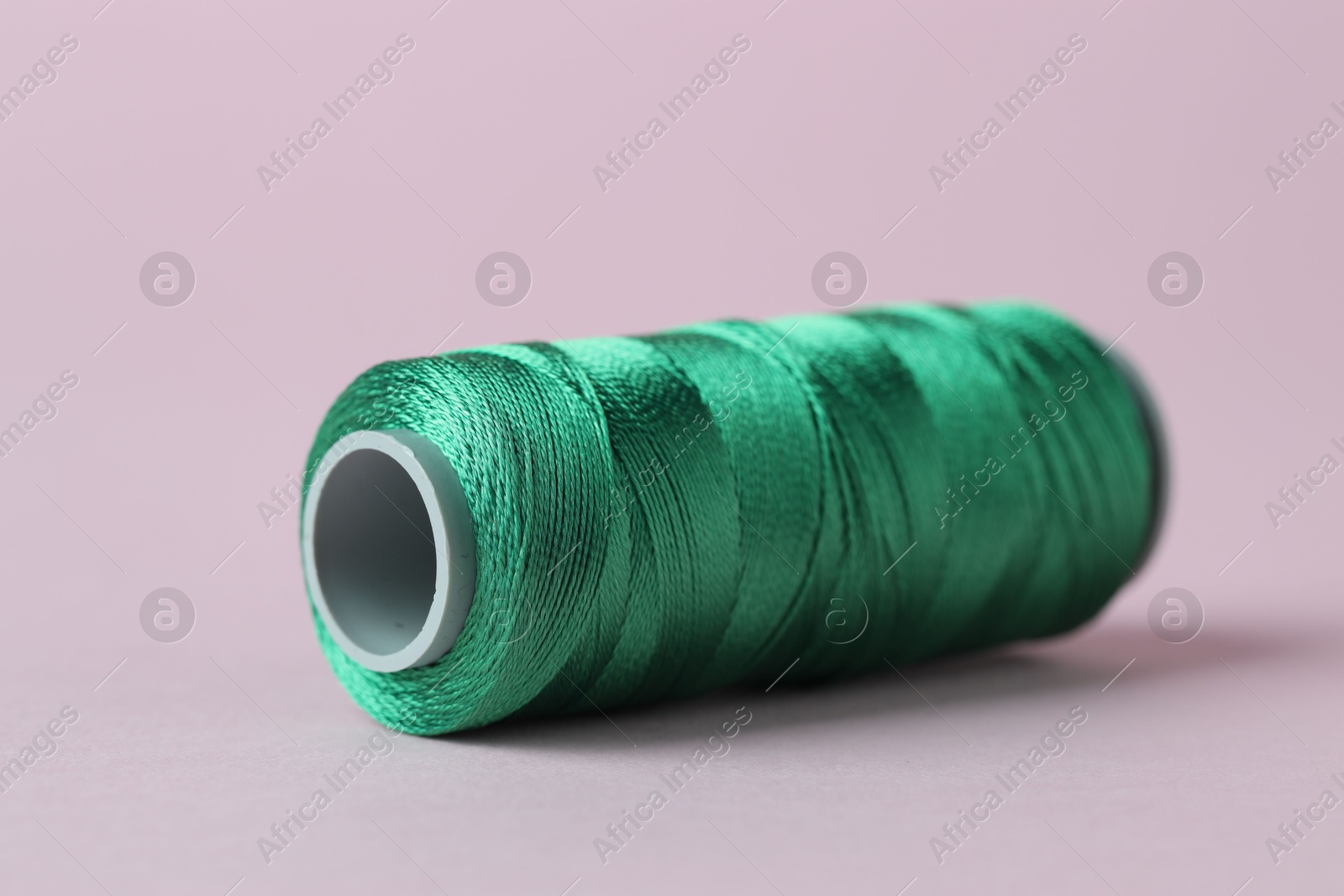 Photo of Spool of green sewing thread on pink background, closeup