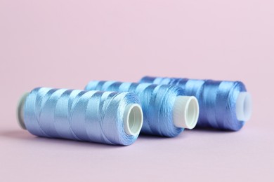 Photo of Spools of light blue sewing threads on pink background, closeup