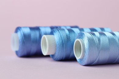 Photo of Spools of light blue sewing threads on pink background, closeup