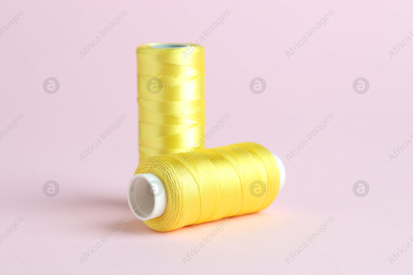 Photo of Spools of yellow sewing threads on pink background, closeup