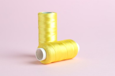 Photo of Spools of yellow sewing threads on pink background, closeup