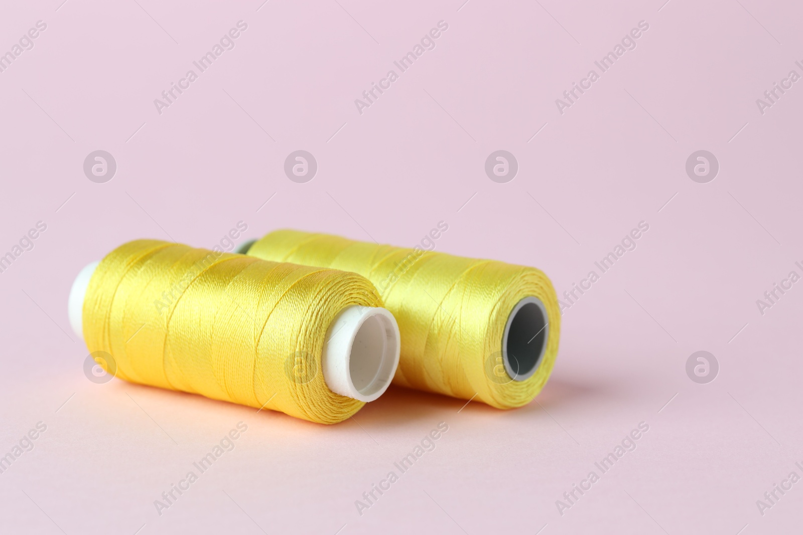 Photo of Spools of yellow sewing threads on pink background, closeup. Space for text