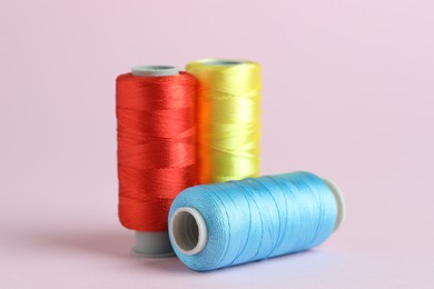 Photo of Spools of colorful sewing threads on pink background, closeup