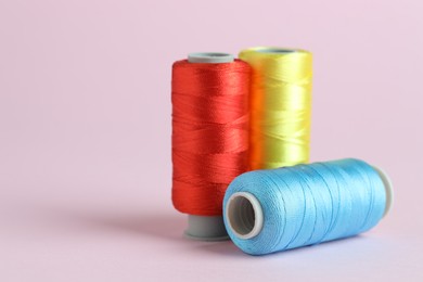 Photo of Spools of colorful sewing threads on pink background, closeup. Space for text