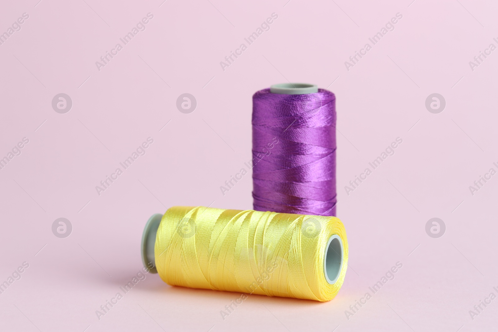 Photo of Spools of colorful sewing threads on pink background