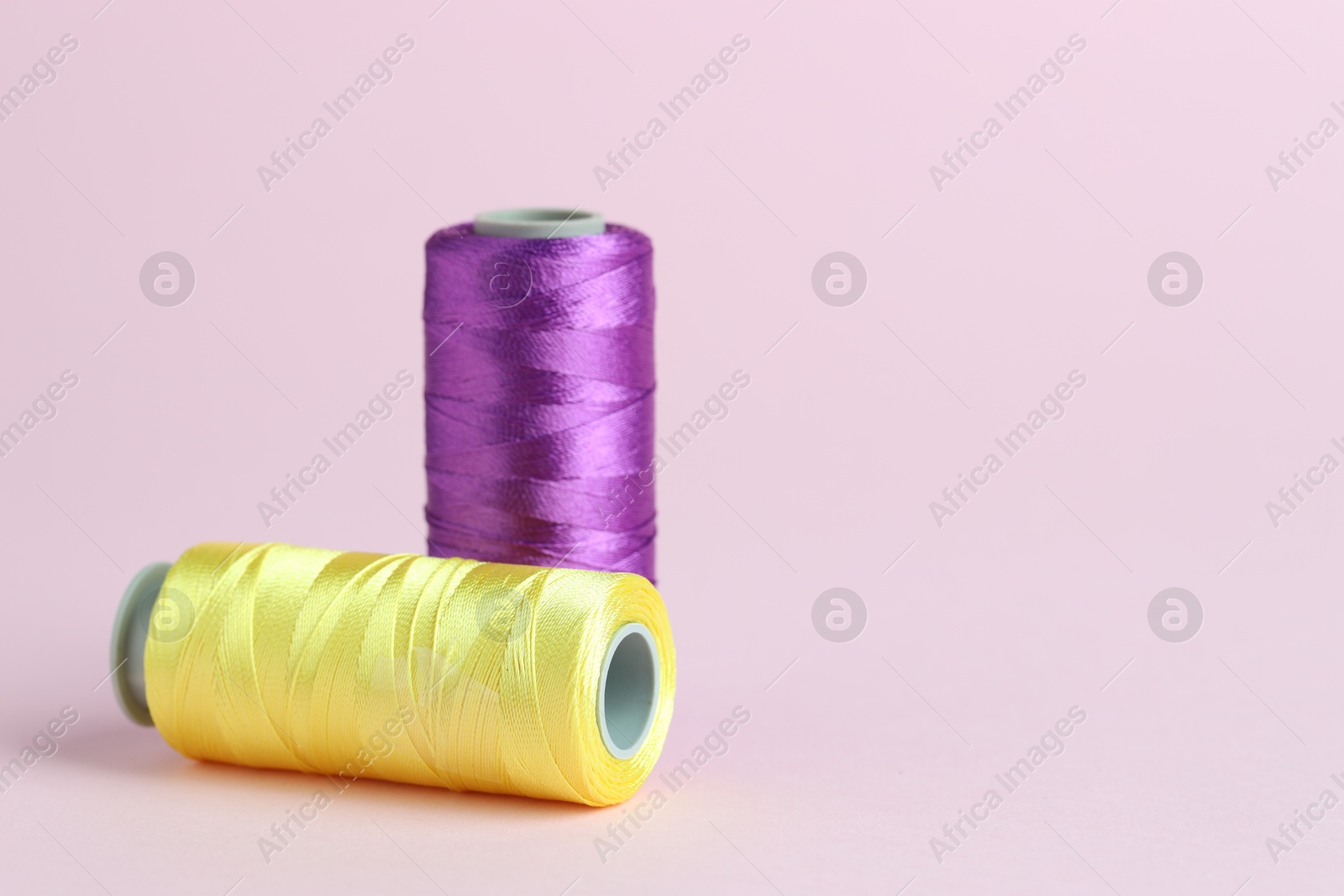 Photo of Spools of colorful sewing threads on pink background, space for text