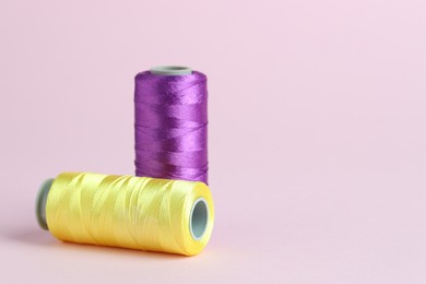 Photo of Spools of colorful sewing threads on pink background, space for text