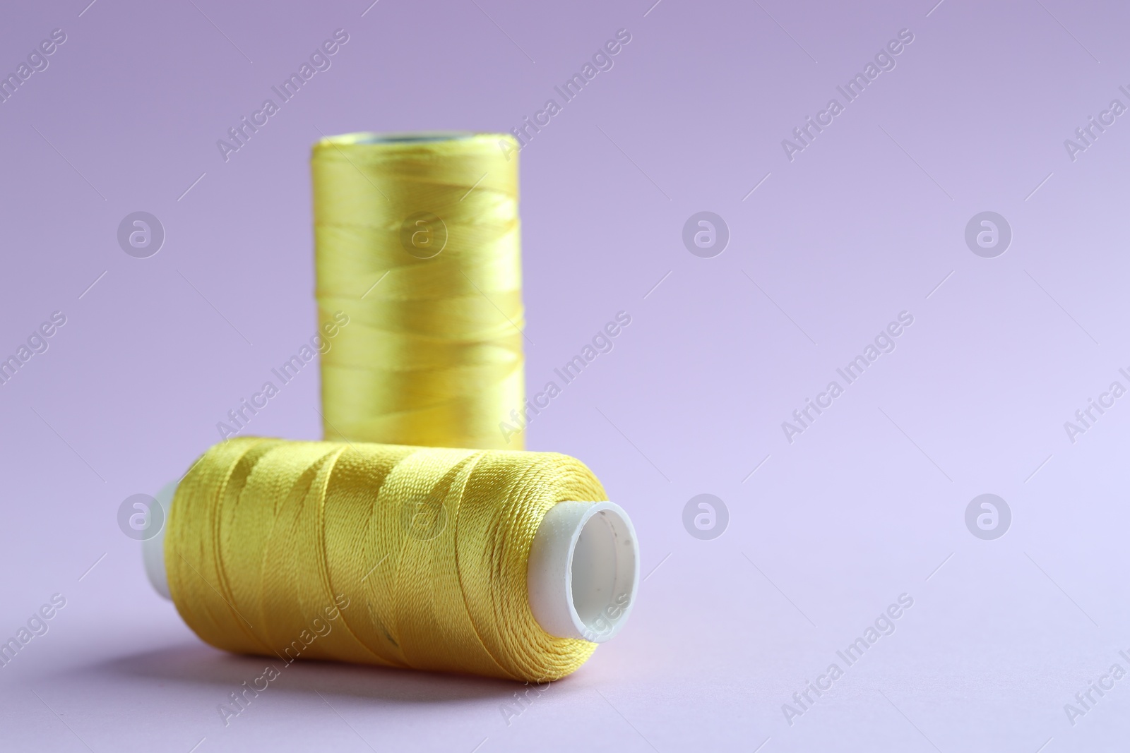 Photo of Spools of yellow sewing threads on lilac background, closeup. Space for text