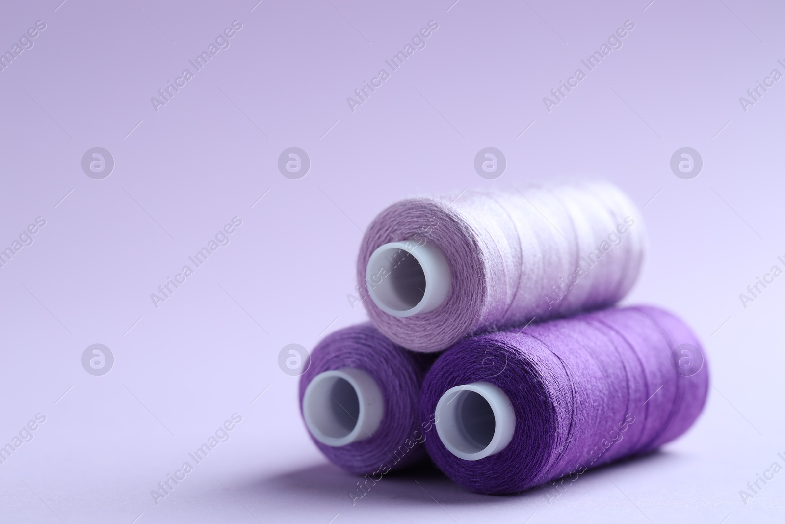 Photo of Spools of colorful sewing threads on lilac background, closeup. Space for text