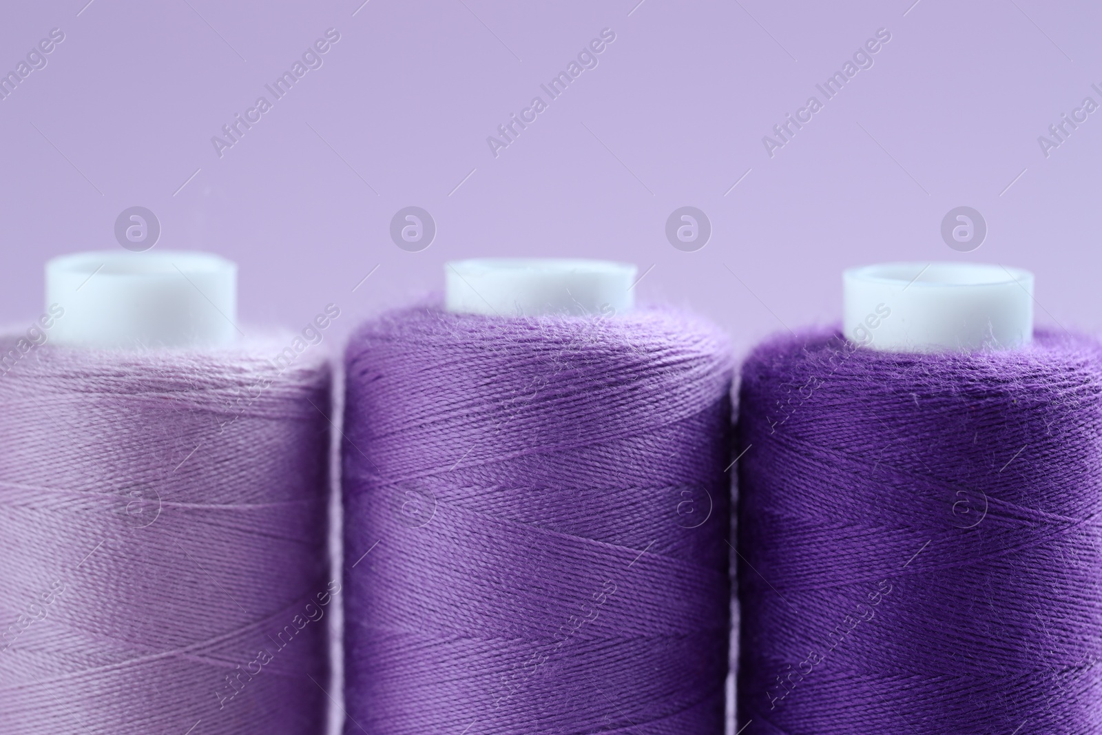 Photo of Spools of colorful sewing threads on lilac background, closeup