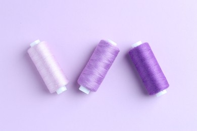 Photo of Spools of colorful sewing threads on lilac background, flat lay