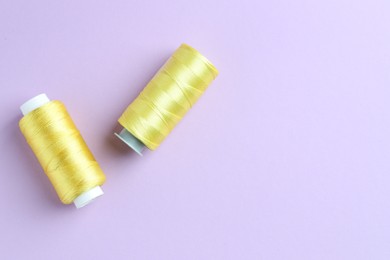 Photo of Spools of yellow sewing threads on lilac background, top view. Space for text